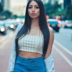 Confident woman walking on vibrant city street, showcasing modern fashion in denim and crop top.